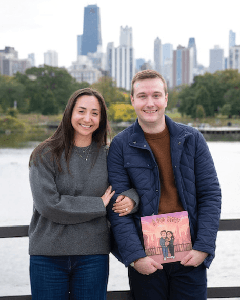 Una pareja sonriente junto al lago, con los rascacielos de la ciudad detrás, sosteniendo su libro de boda personalizado con su ilustración en la portada